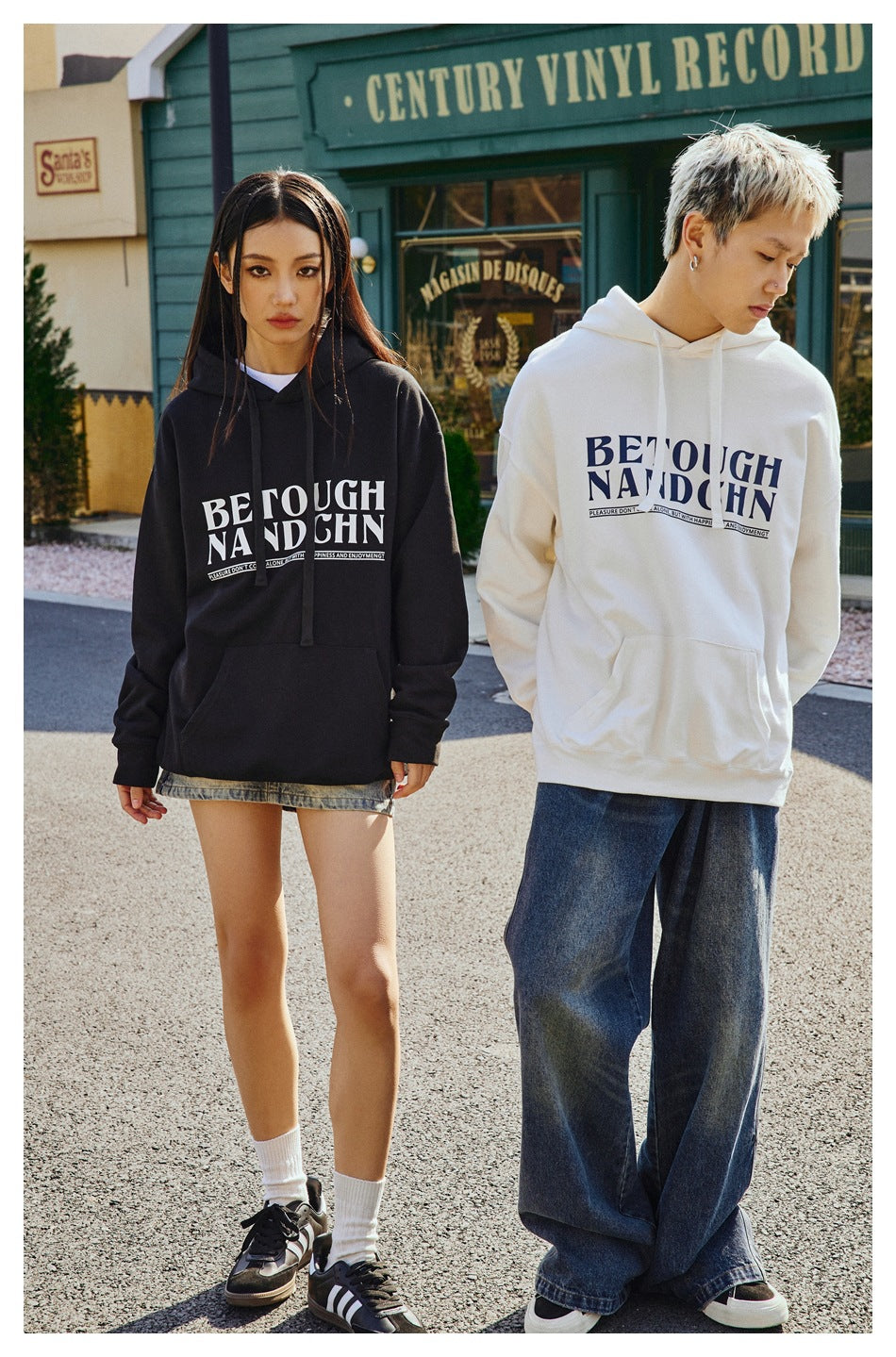 Models wear black and white graphic pullover hoodies; the black hoodie has drawstrings, while the white one has a kangaroo