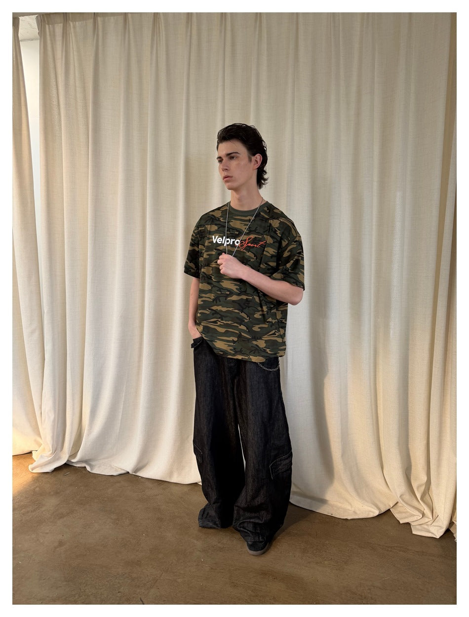Model wearing a dark green camouflage graphic T-shirt with loose black trousers.