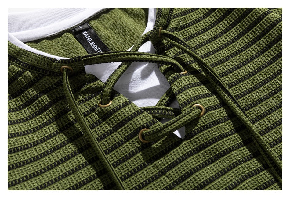 Close-up of olive-green and black striped fabric with cord lacing, brass-tone eyelets, and white neckline trim.