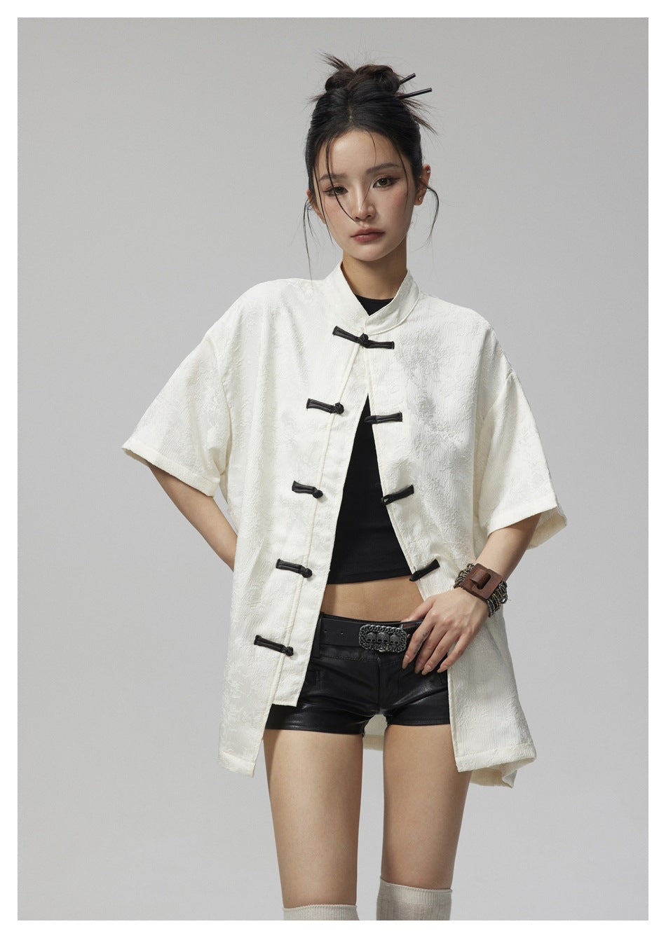 Front view of a model wearing an ivory short-sleeve jacket with black frog closures, a black top, and black shorts.