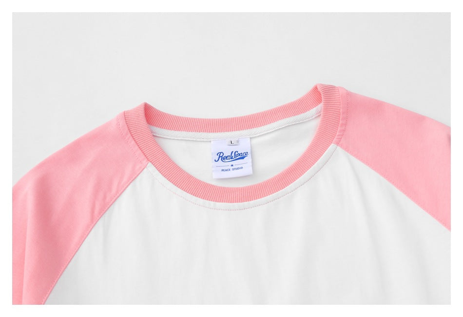 Close-up of a white raglan T-shirt with pink sleeves, pink ribbed neckline and a visible inner label.