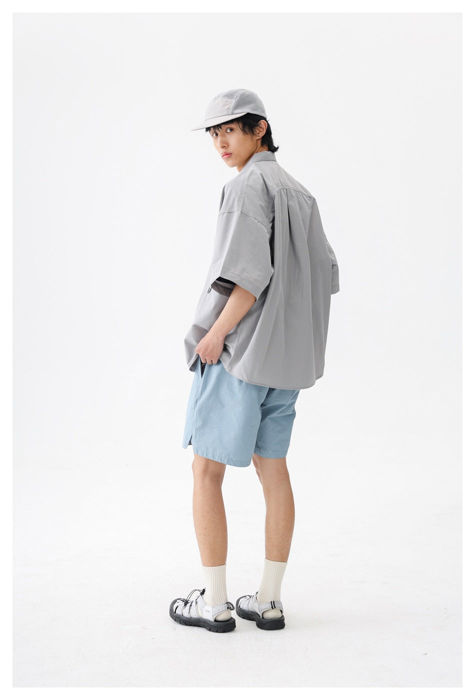 Model in a light gray short-sleeve shirt and blue shorts, shown from a rear three-quarter angle.
