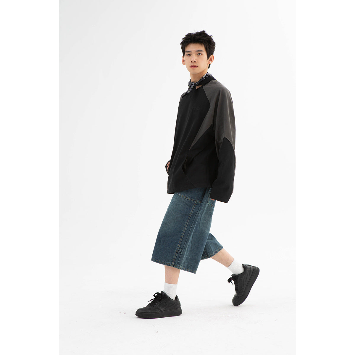 Model in a black sweatshirt with charcoal panels, shown at an angle with a denim skirt and sneakers.