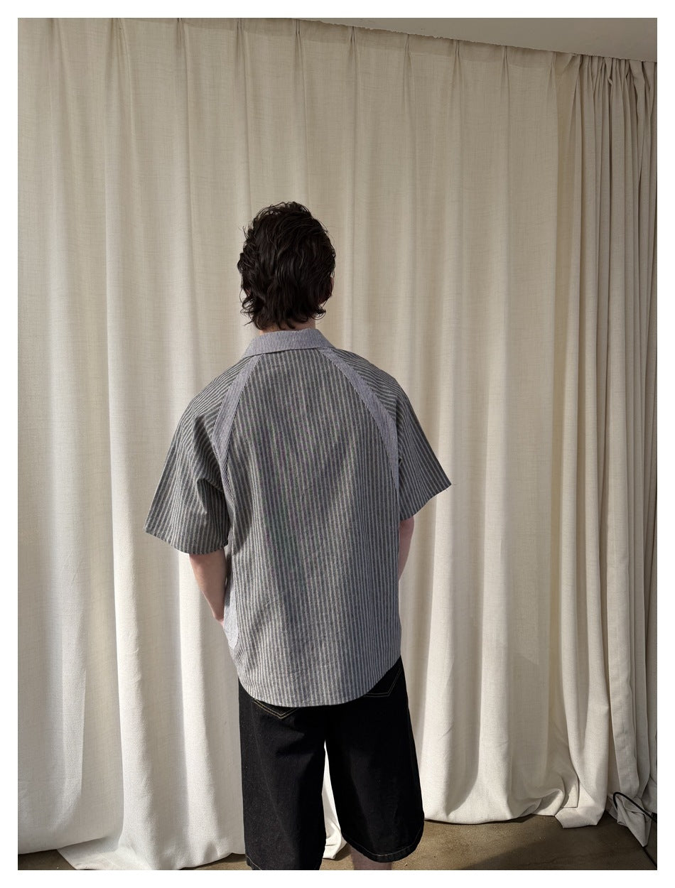 Back view of a model wearing a gray striped short-sleeve button-up shirt and black shorts.