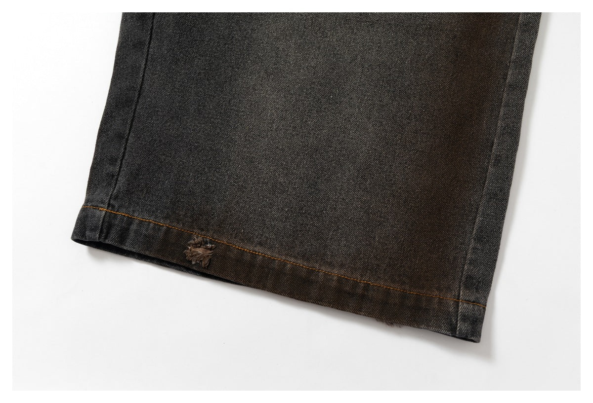Close-up of a dark charcoal denim hem with brown contrast stitching and a small worn embroidered motif.