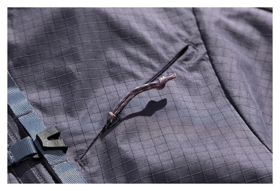 Close-up of a cord toggle on a charcoal grid-pattern jacket beside a webbing strap and buckle.