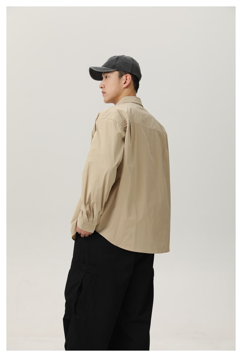 Three-quarter rear view of a model wearing a beige long-sleeve shirt and loose black cargo pants.