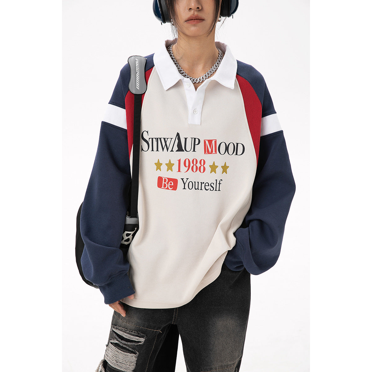 Close-up front view of a model wearing an oversized cream polo sweatshirt with navy and red panels and graphic lettering.