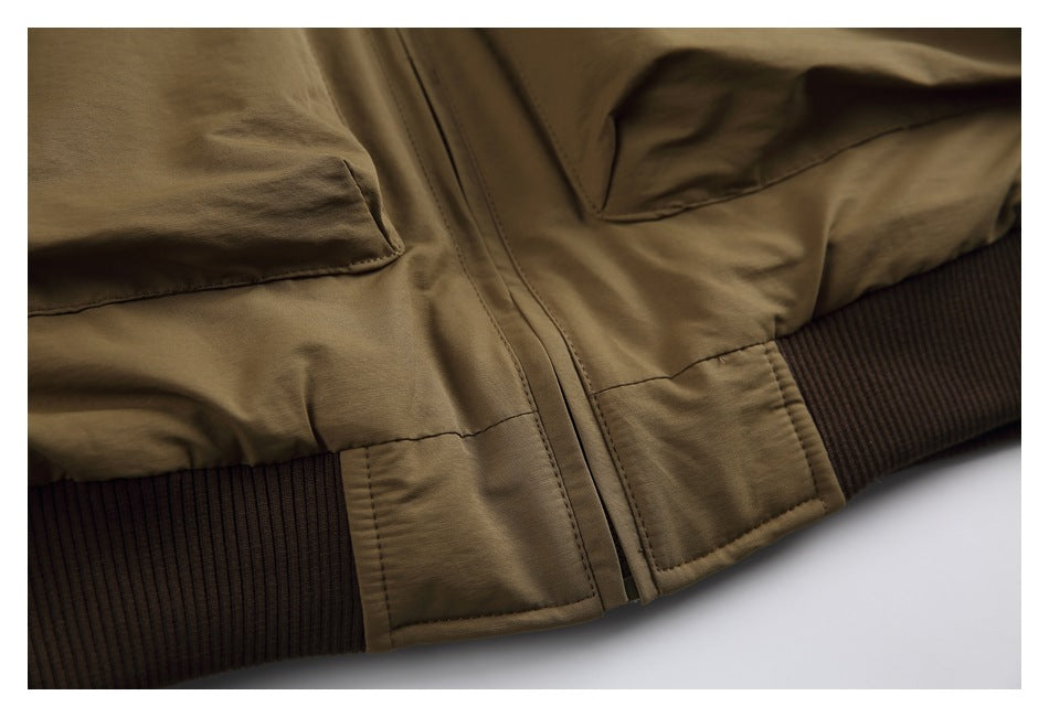 Close-up of an olive-brown jacket front zipper, lower pockets and dark brown ribbed waistband.