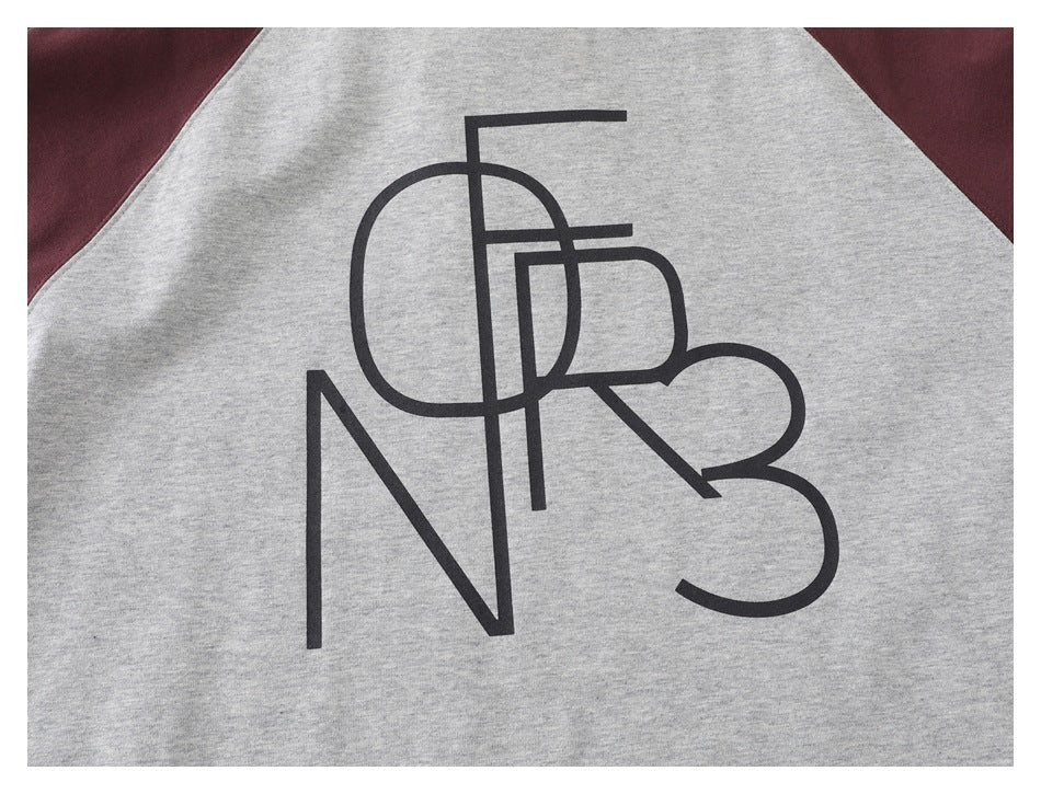 Close-up of a gray garment with burgundy panels and a large black abstract letter print.