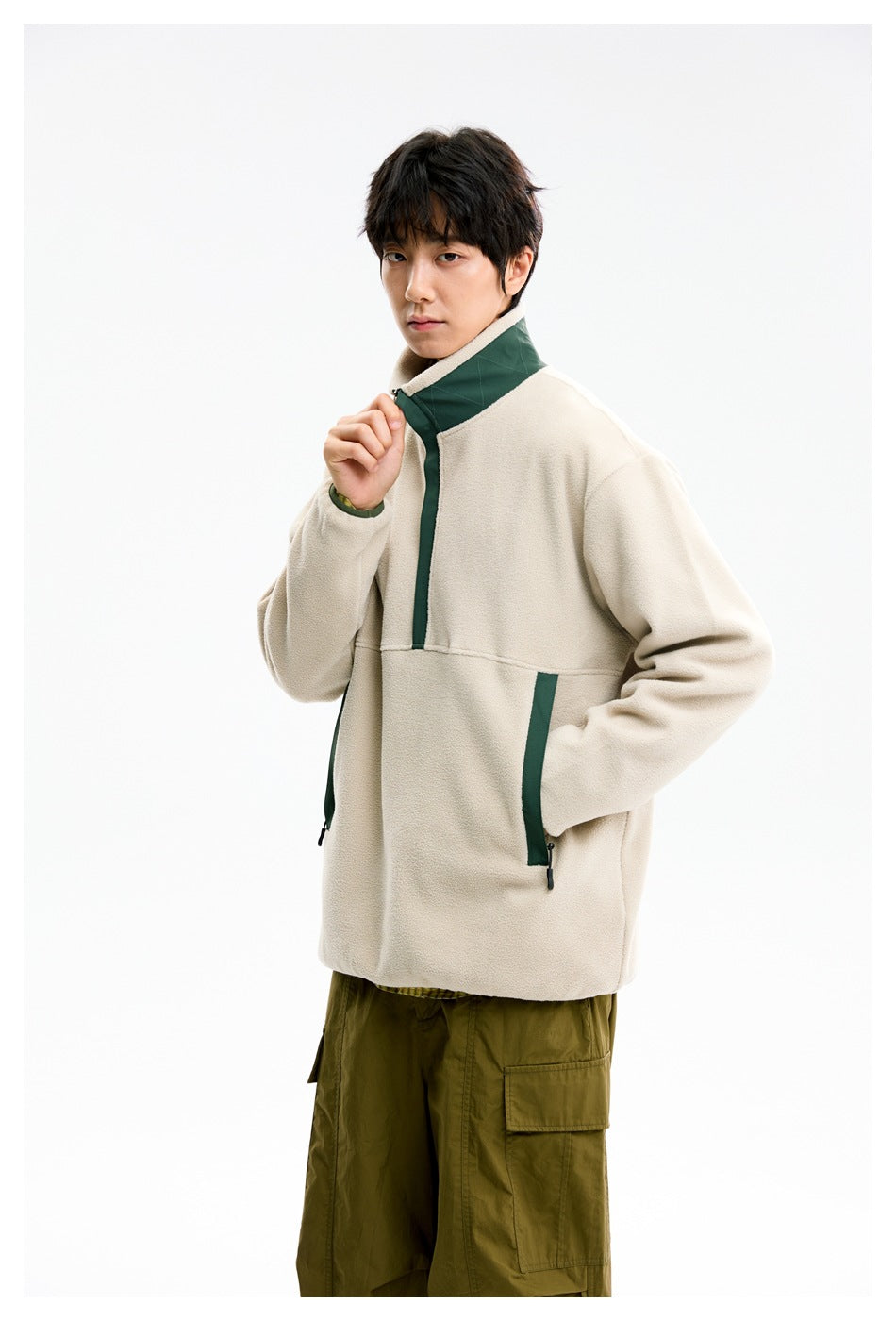 Model wearing a cream fleece pullover with a dark green stand collar, trim and zip pockets, paired with olive cargo pants.