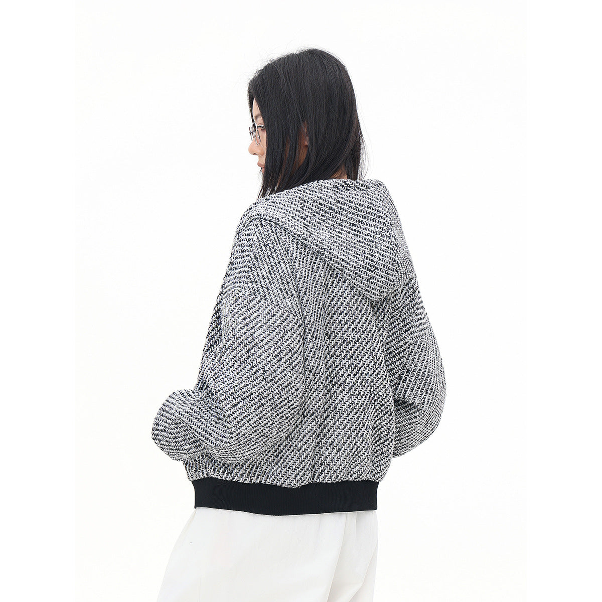 Rear three-quarter view of a model wearing a black-and-white textured hooded jacket with a dark ribbed hem.