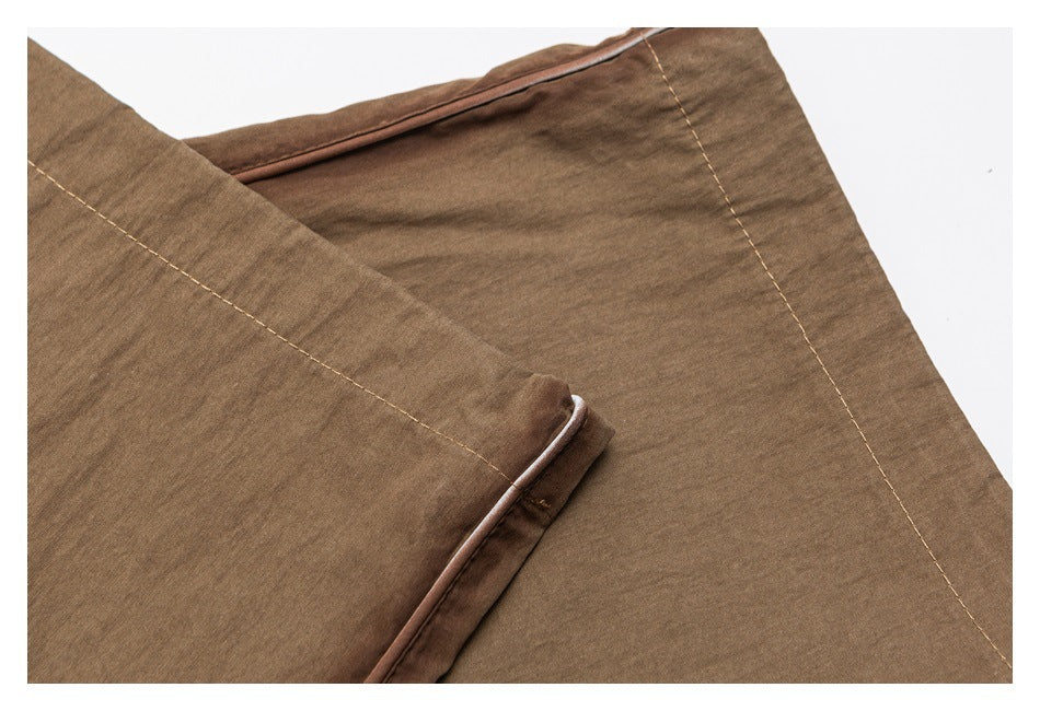 Close-up of brown trousers showing stitched seams and narrow contrasting edge trim.