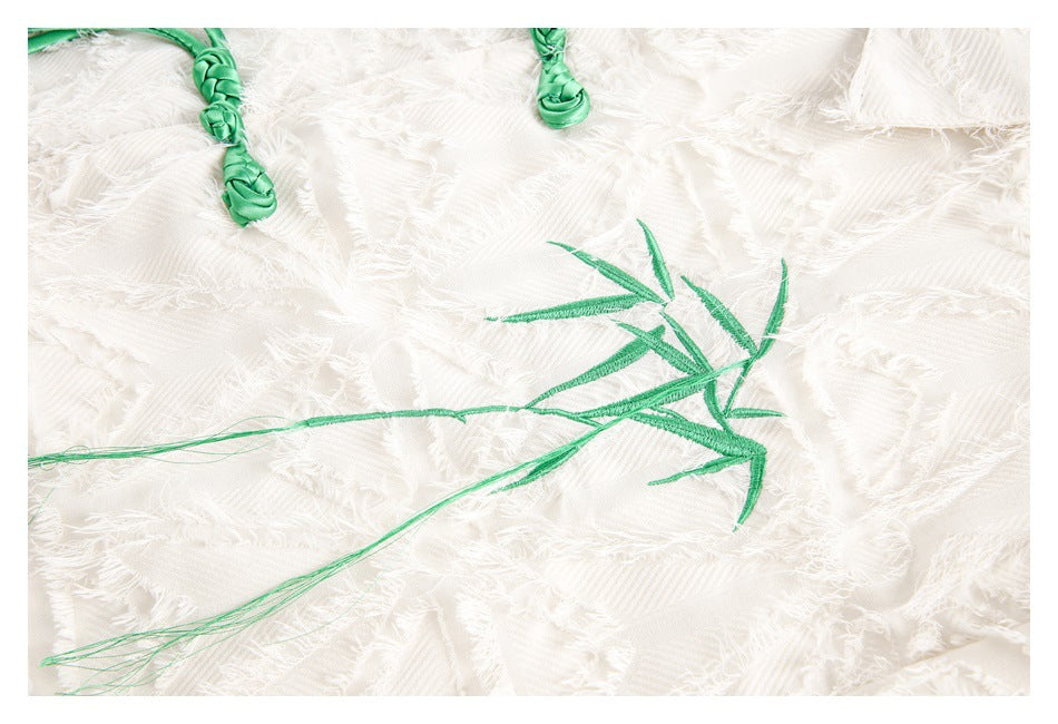 Close-up of ivory fringed fabric with green bamboo embroidery and knotted green accents.