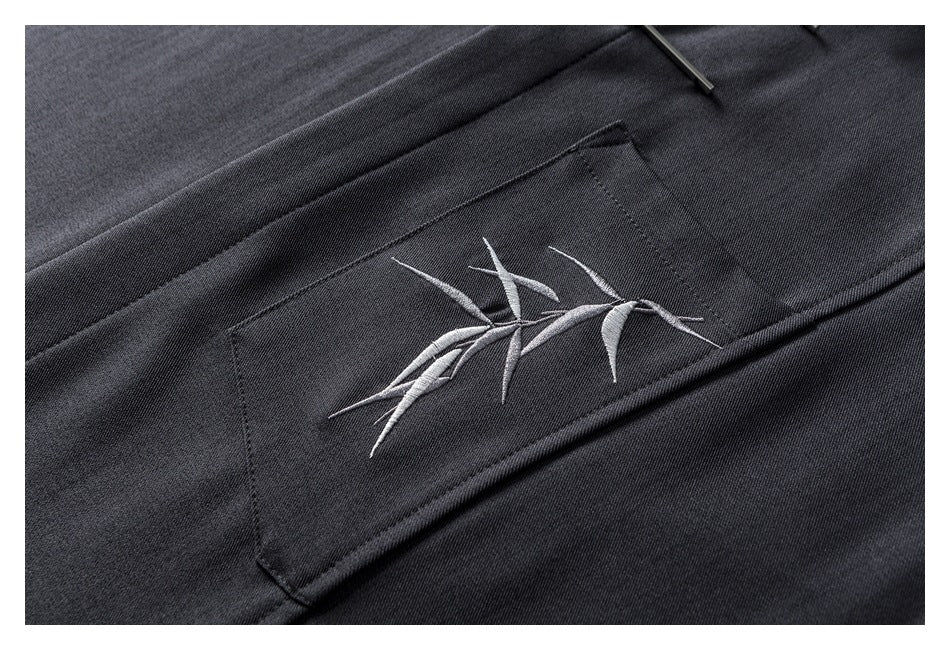 Close-up of pale bamboo embroidery on the chest pocket of a charcoal shirt.
