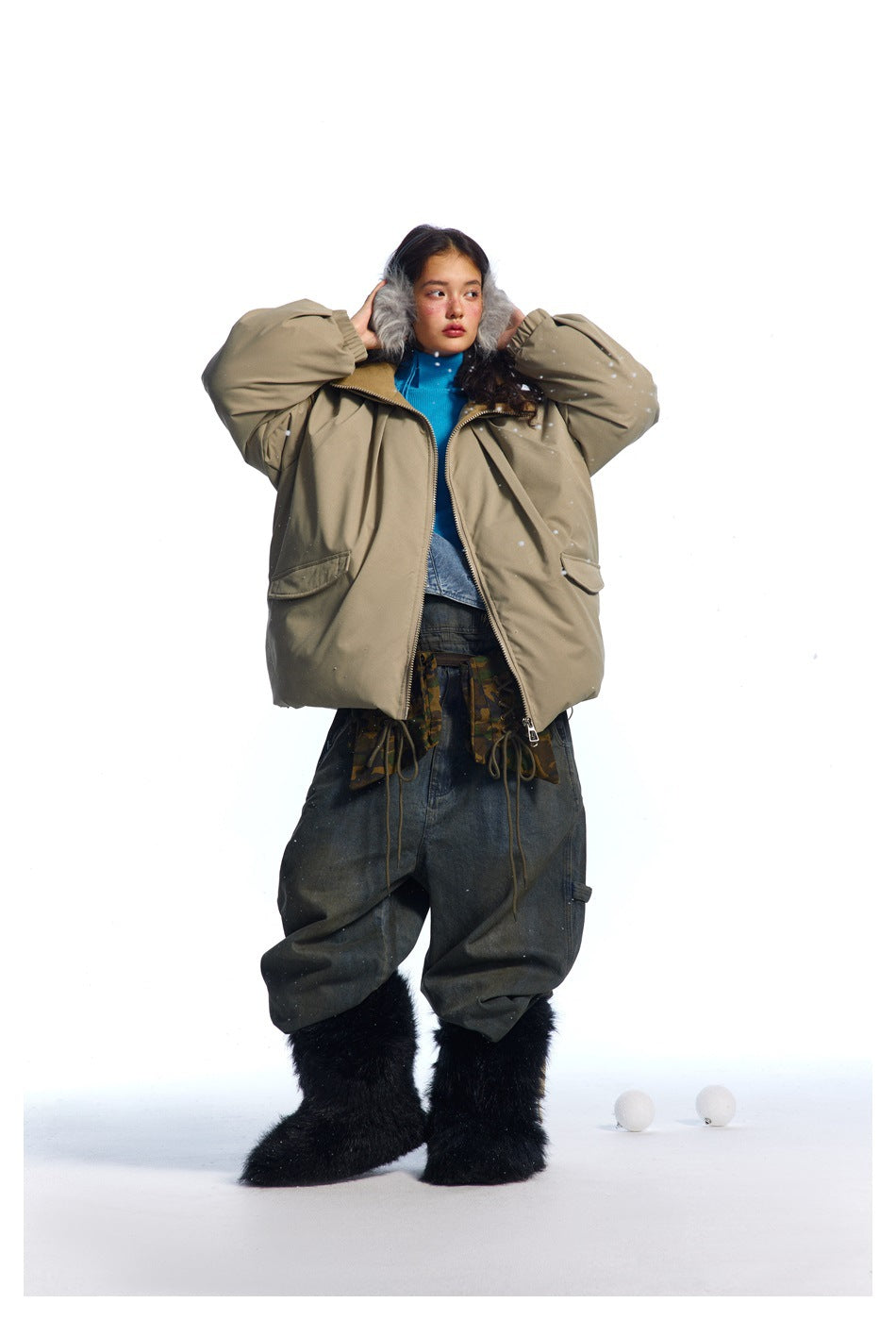 Model wearing an open taupe oversized jacket with a high collar and flap pockets, styled with dark baggy pants and furry
