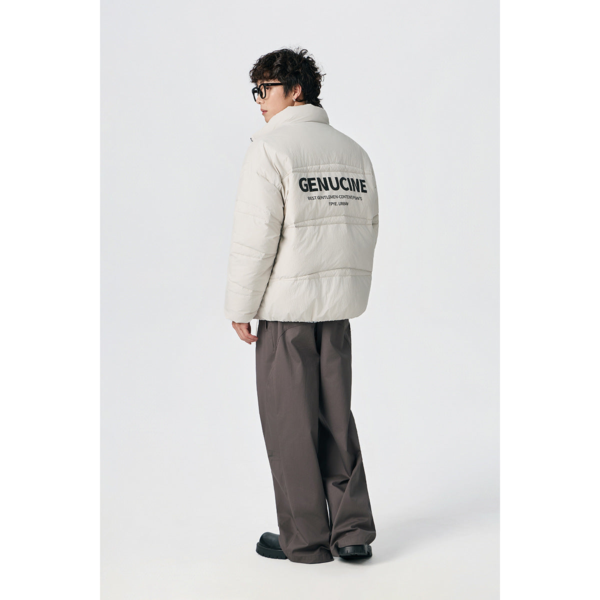 Model wearing an ivory puffer jacket, shown from behind with large black lettering, and dark wide-leg trousers.