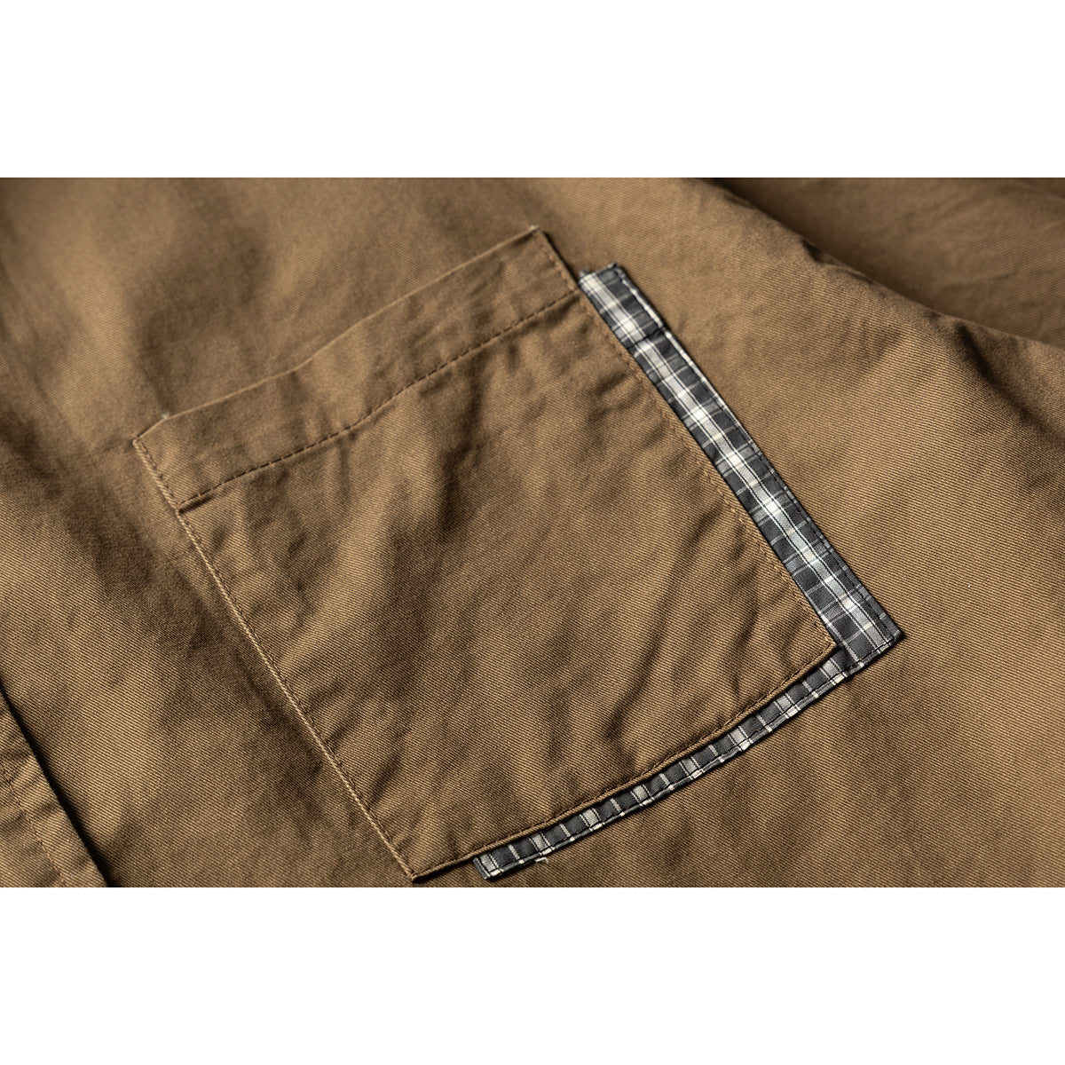 Close-up of a brown shirt's chest pocket edged with dark plaid fabric.