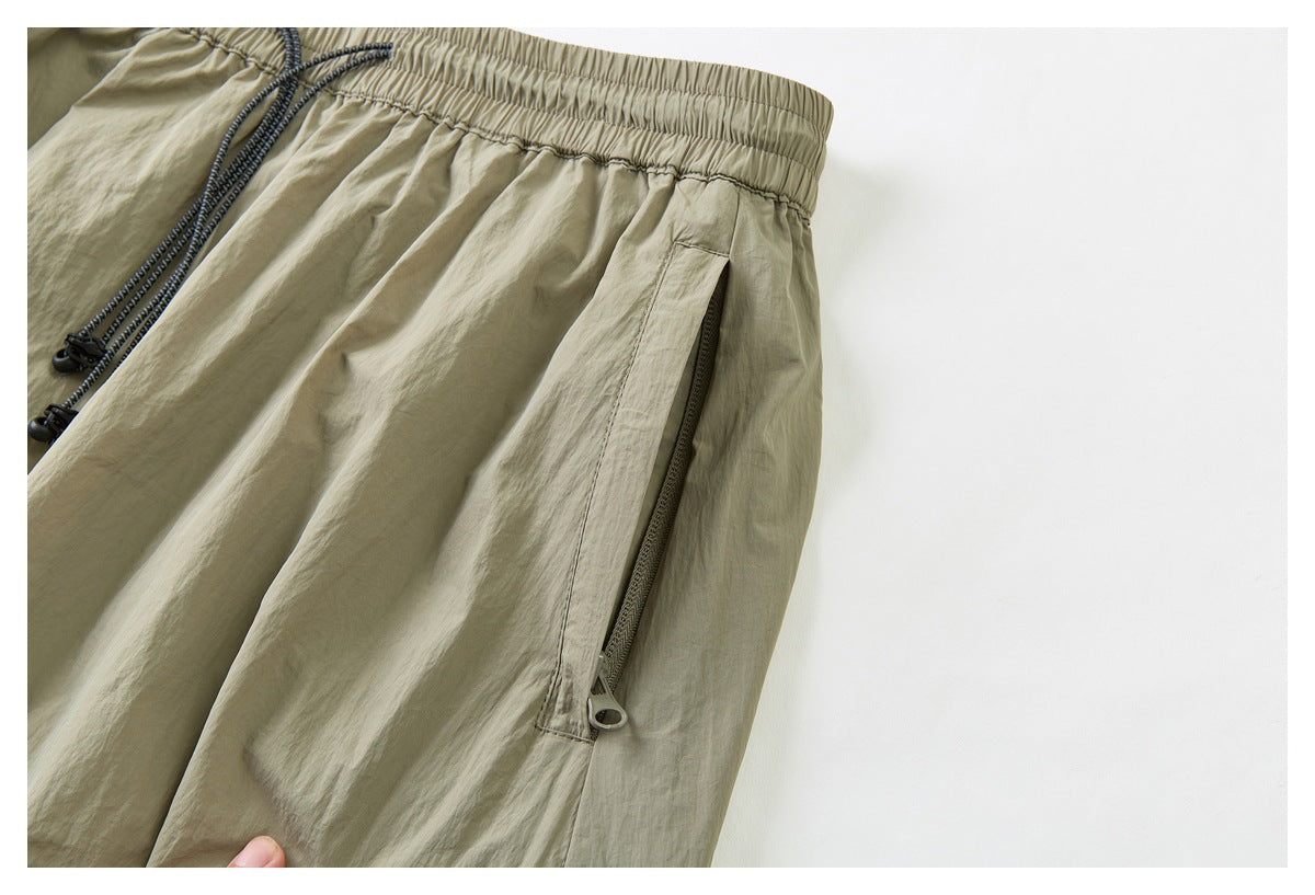Close-up of khaki shorts showing an elastic waistband, dark drawcords, and a vertical zip pocket.