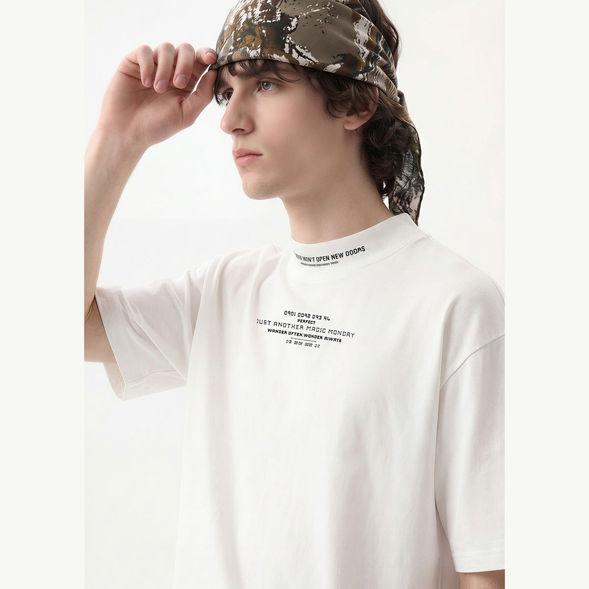 Close-up of a model in a white oversized T-shirt with small black text at the chest and collar, wearing a camouflage