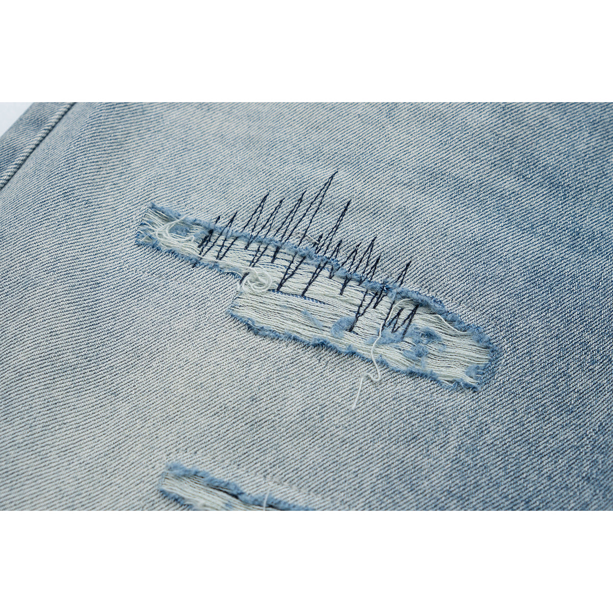 Close-up of a frayed horizontal rip with dark stitch accents on light-wash denim.