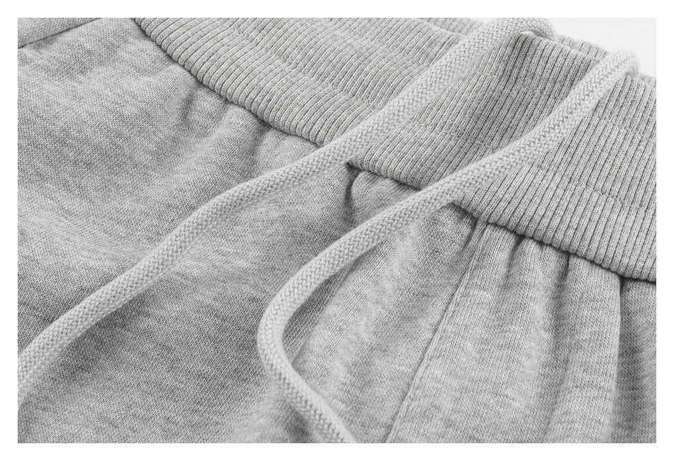 Close-up of braided drawstrings crossing the ribbed waistband of light gray sweatpants.