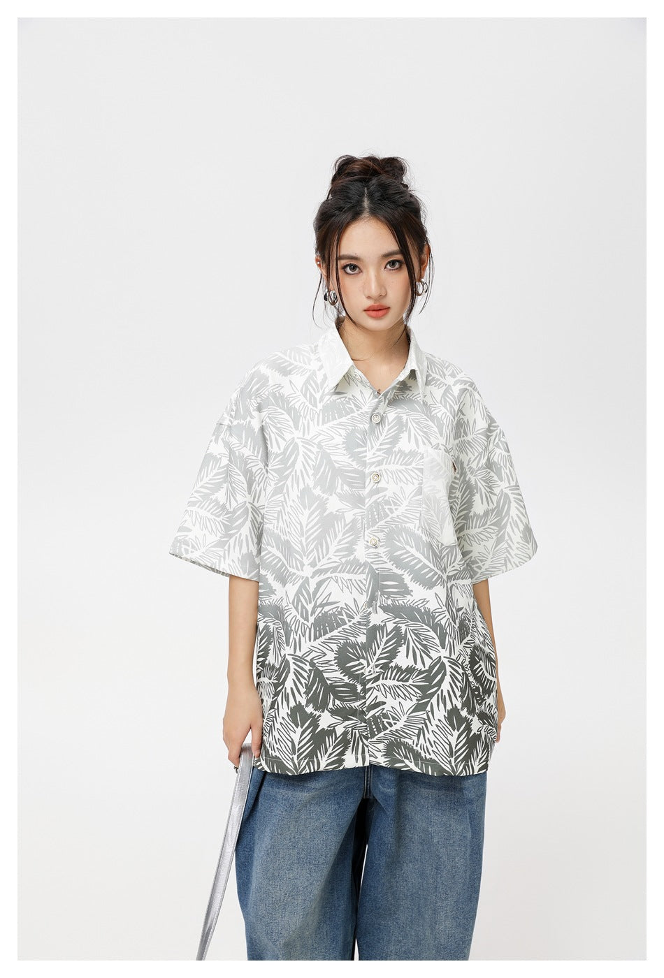 Model wearing an oversized white short-sleeve shirt with gray leafy print and blue jeans, shown from the front.