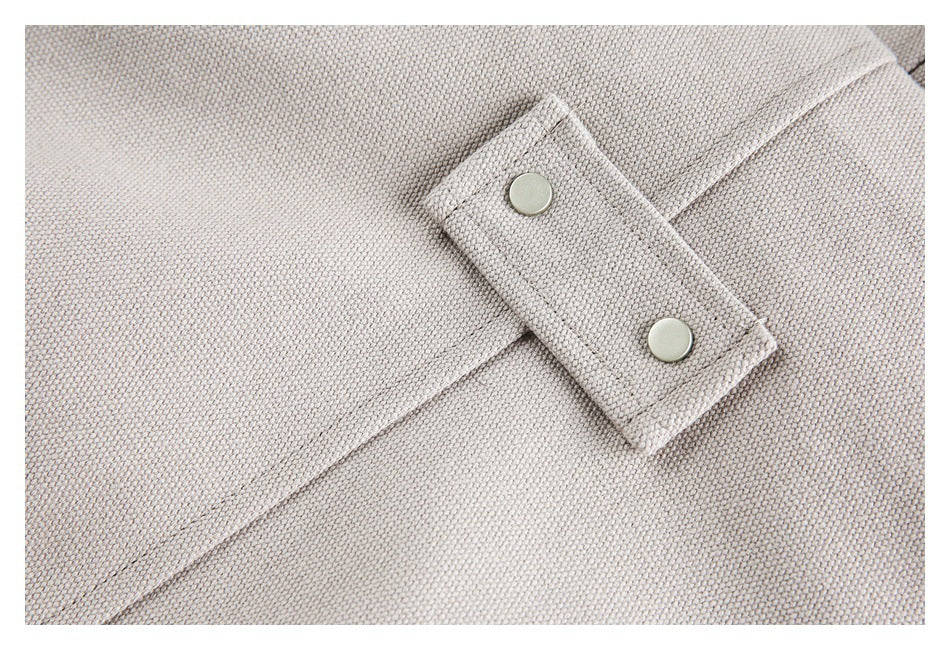 Close-up of a small snap-fastened fabric tab on the pale taupe-gray jacket.