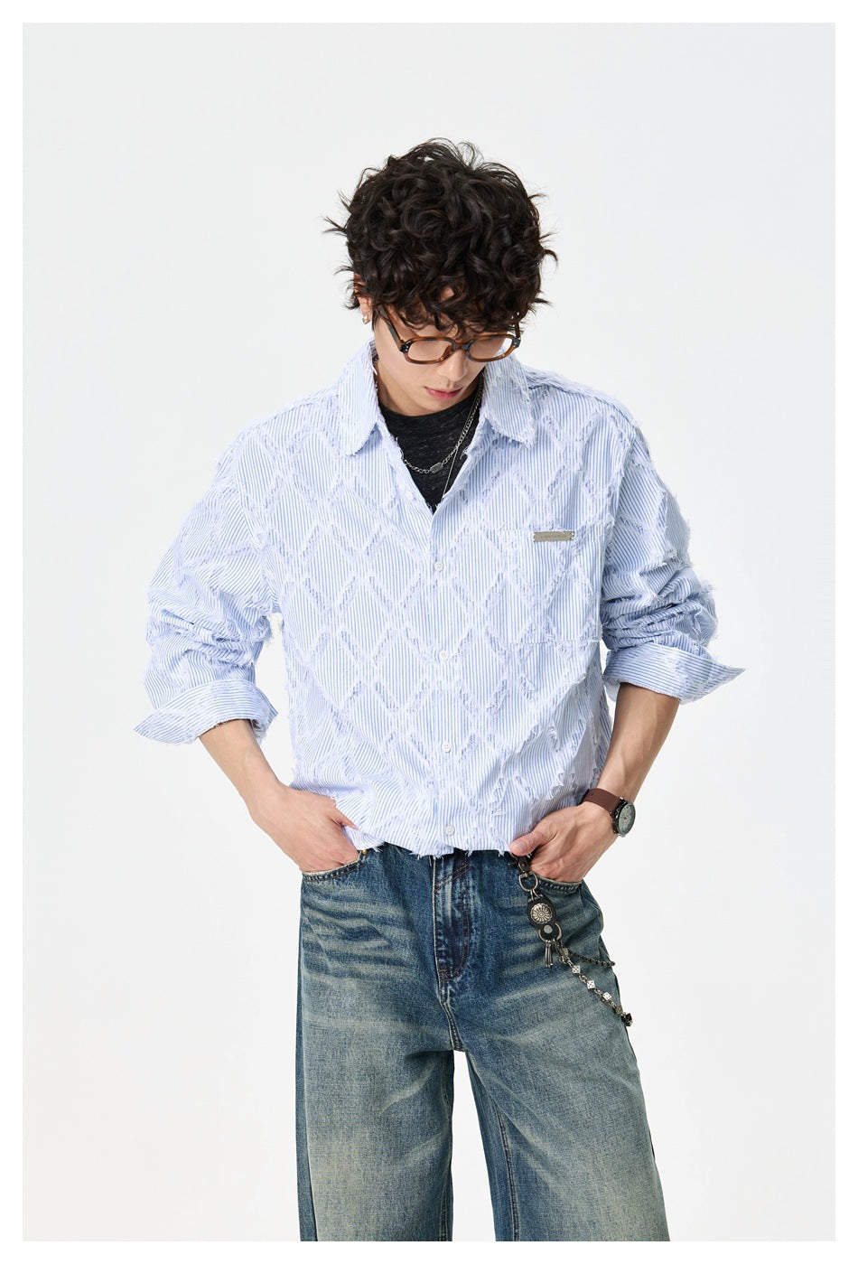 Model in a light blue pinstripe shirt with frayed diamond pattern, hands in pockets of wide-leg jeans