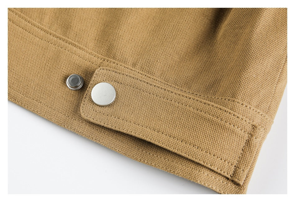 Close-up of a tan garment edge with a silver snap fastening and double-stitched tab.