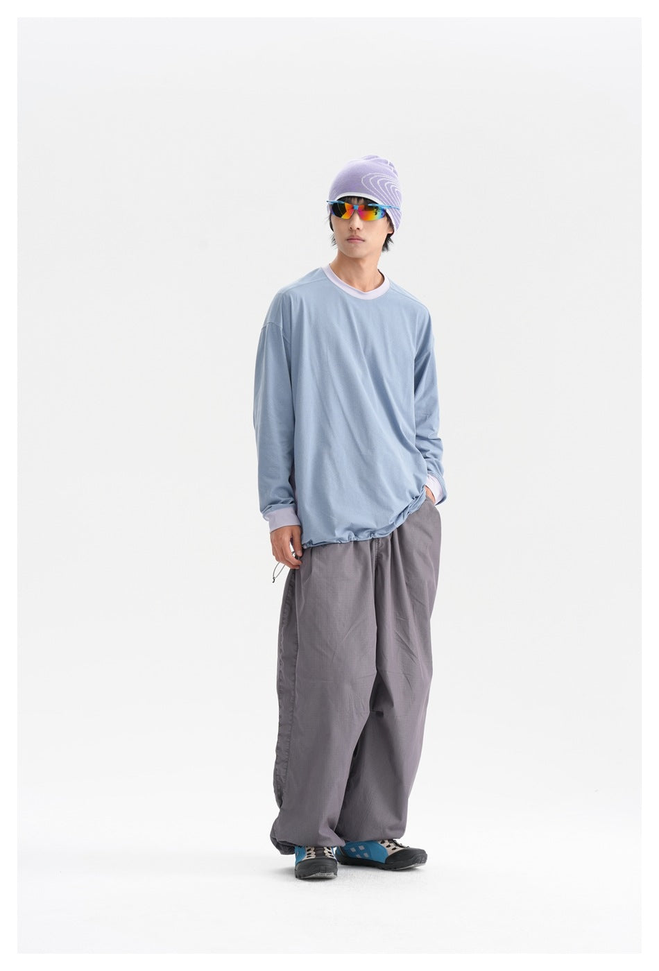 Full-length model wearing an oversized light blue shirt with lavender trim and loose gray trousers.