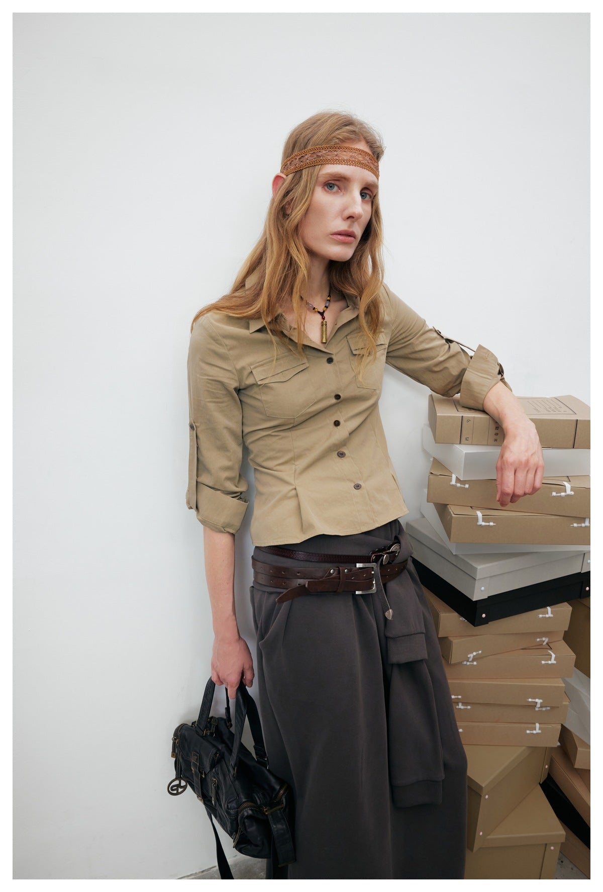 Model wearing a khaki button-up shirt with flap chest pockets and rolled sleeves, paired with dark trousers.