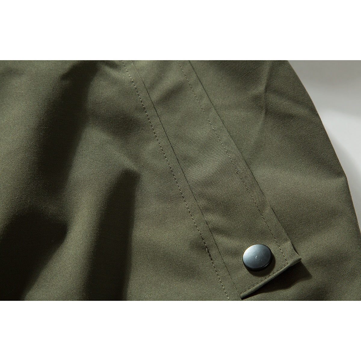 Close-up of an olive-green jacket sleeve tab with a black snap and visible stitching.