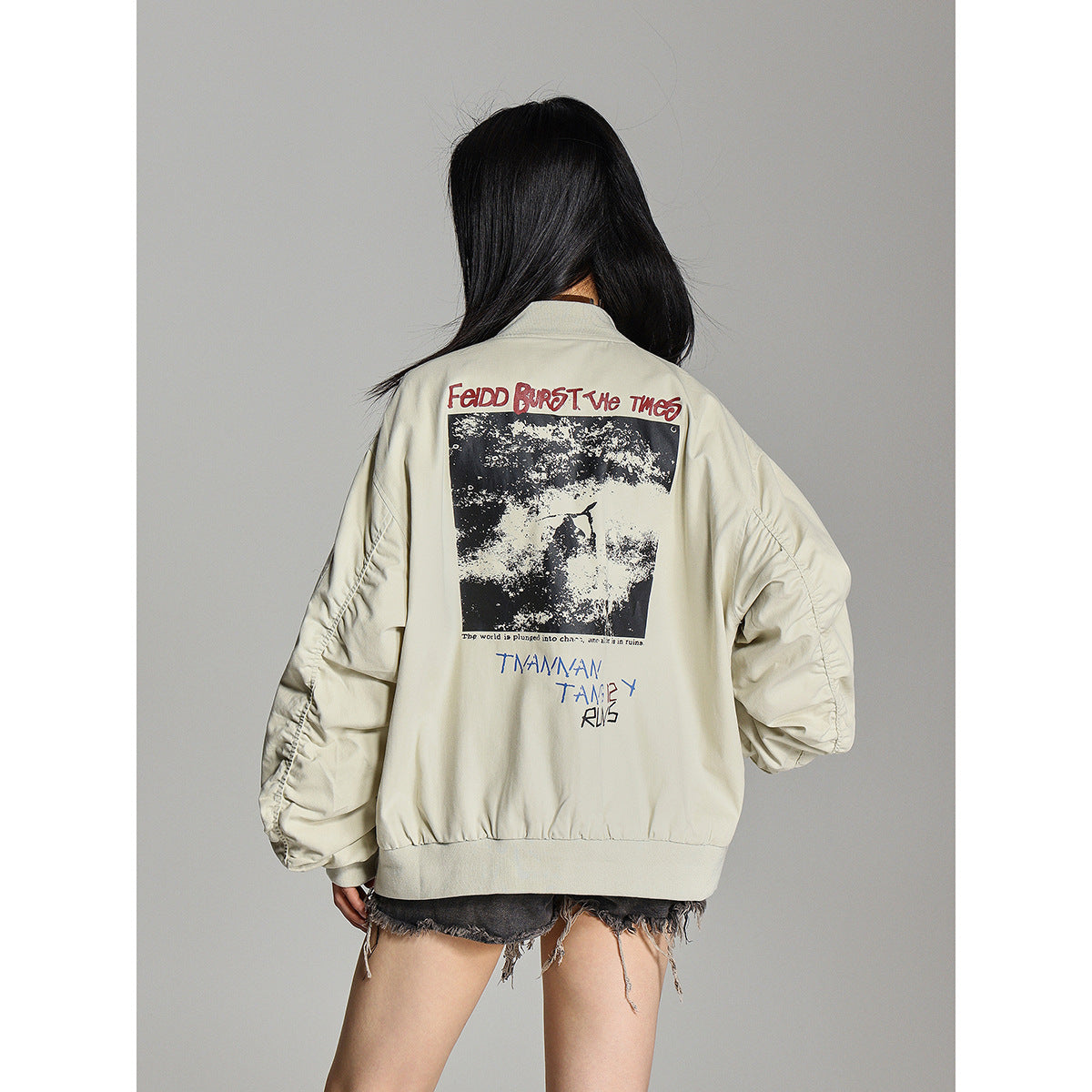 Back view of a model wearing an oversized pale beige bomber jacket with a large graphic print and ribbed hem.