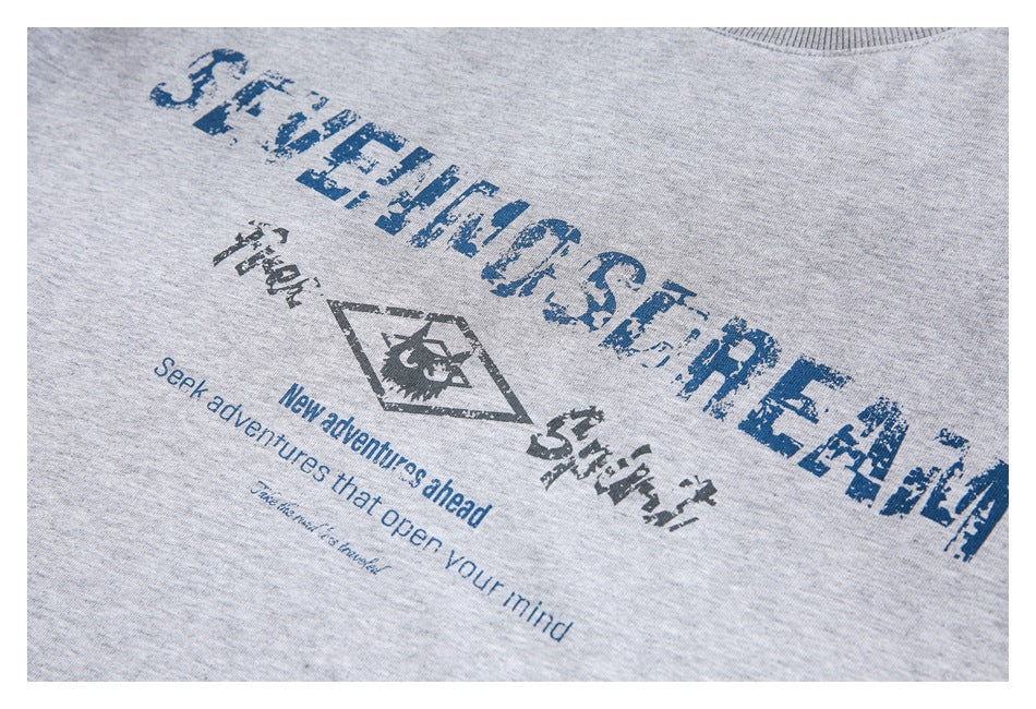 Close-up of a distressed blue and dark graphic with adventure-themed text on a heather gray top.