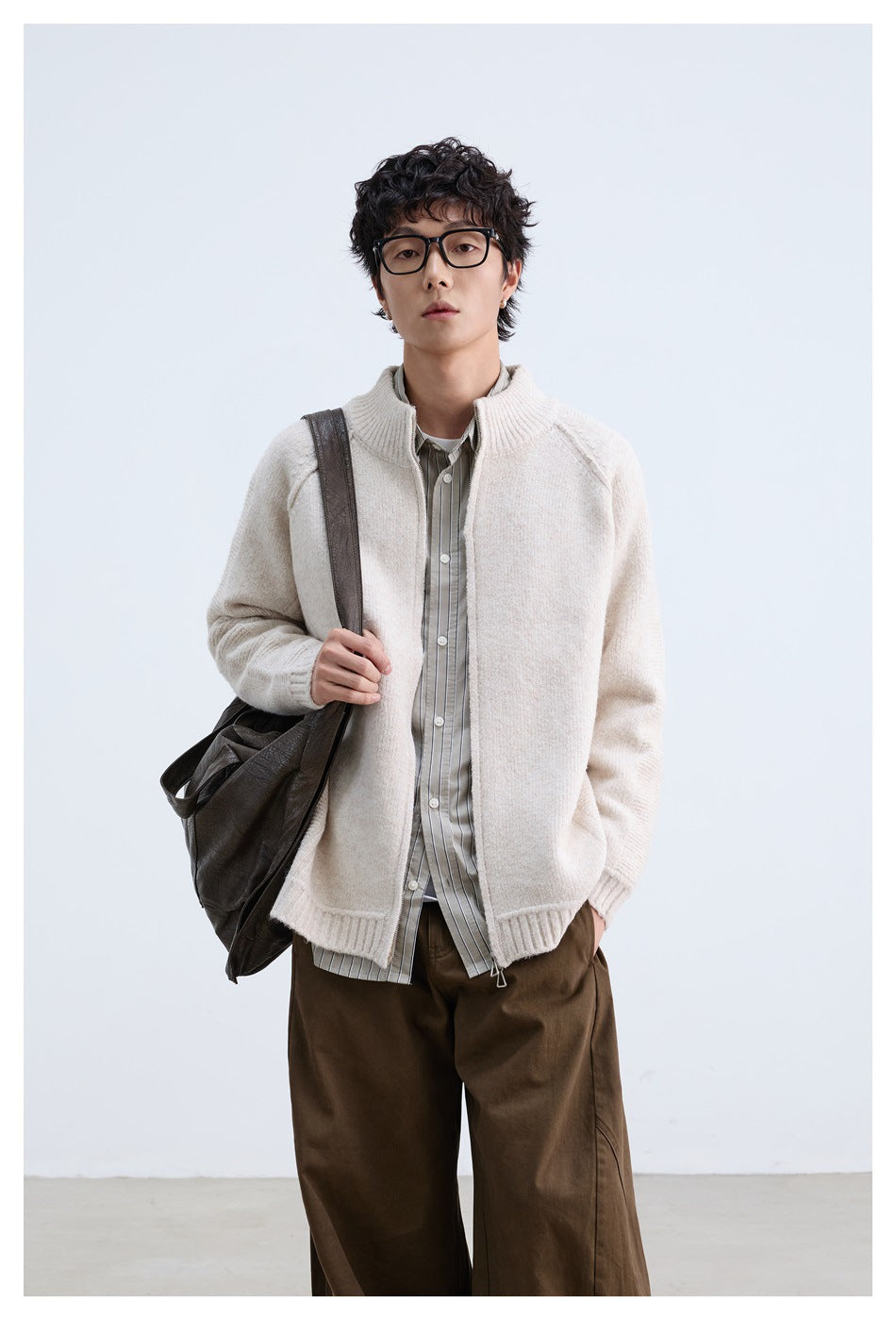 Model wearing an ivory zip-front knit jacket with a ribbed stand collar, styled with a striped shirt and brown trousers.