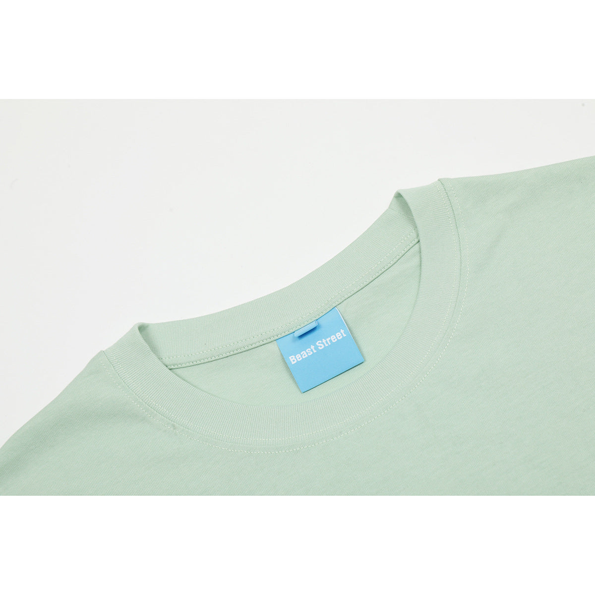 Close-up of a pale mint T-shirt’s ribbed crew neck and blue Beast Street label.