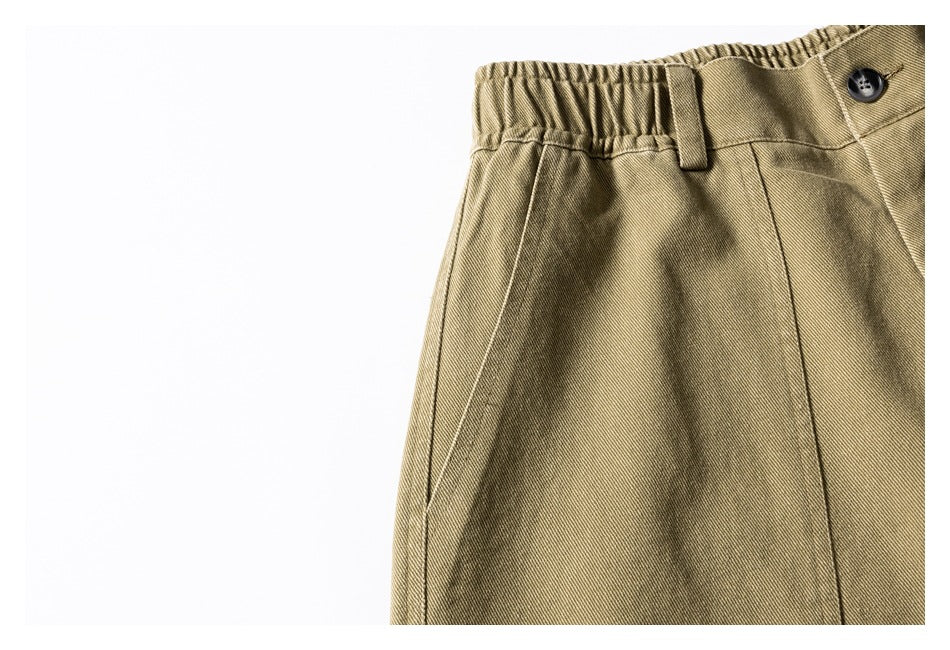 Close-up of khaki trousers showing the elastic waistband, belt loop, dark button, and front seam.