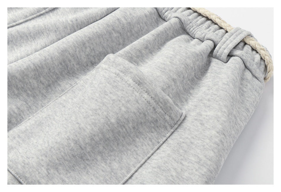 Close-up of light gray heathered sweatpants showing a front patch pocket, elastic waistband, and cream drawstring.