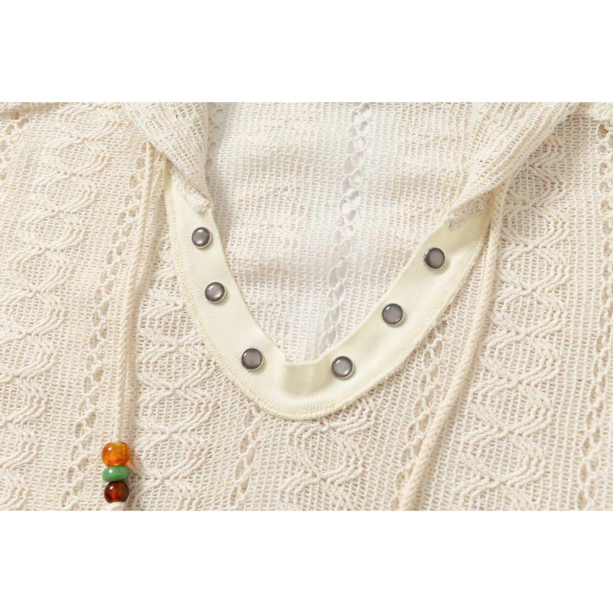 Close-up of the cream open-knit hoodie’s V-neck trim with six metal snaps.