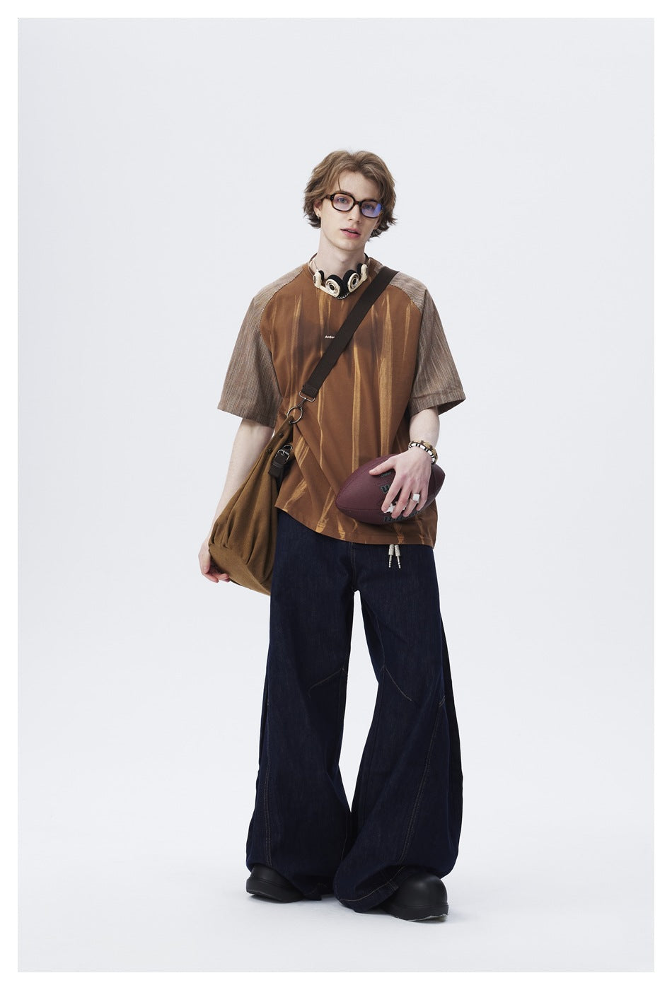 Model wearing a brown striped raglan shirt with gray patterned sleeves and wide dark jeans.