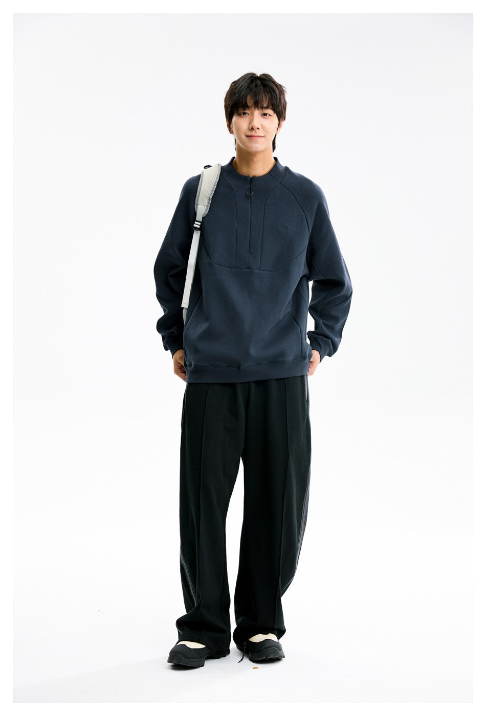 Front view of a model wearing a dark navy high-neck pullover with a short zipper and black wide-leg pants.
