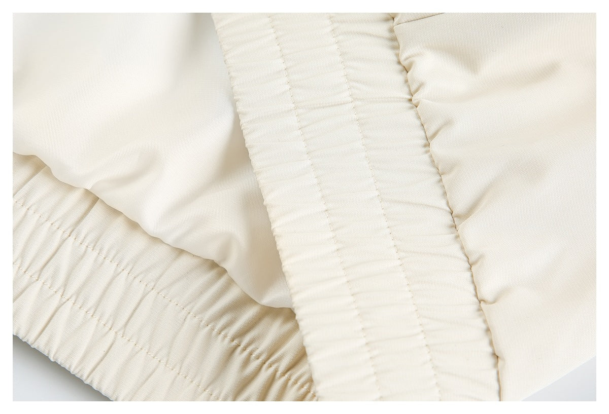 Close-up of ivory garment fabric with a wide gathered elastic band and stitched seams.