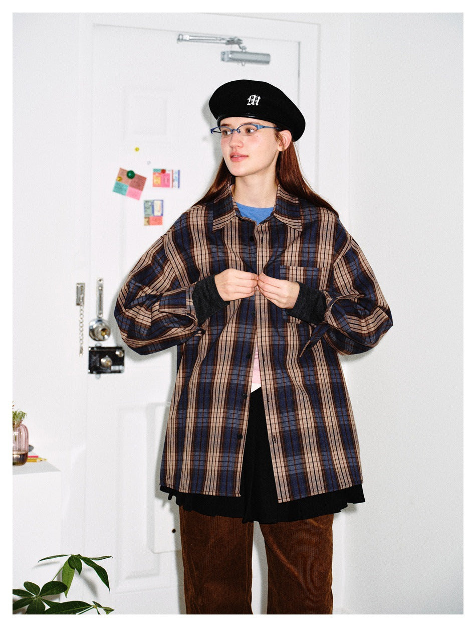 Model in loose plaid long-sleeve shirt with black beret, black pleated skirt and brown corduroy pants, looking aside