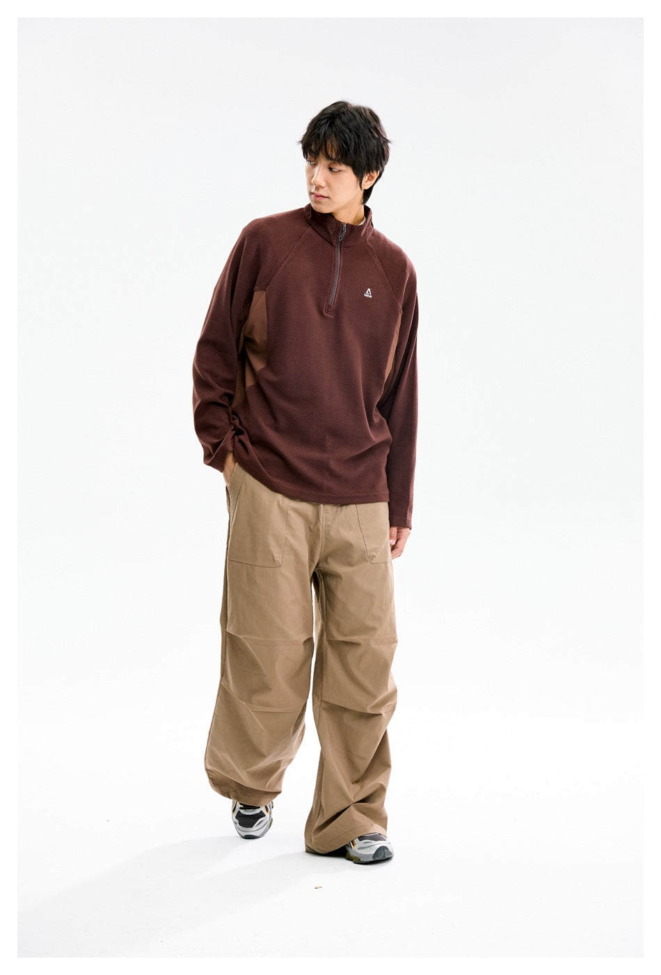 Model wearing a burgundy quarter-zip pullover and loose tan pants, looking to the side.