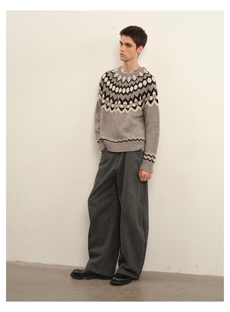 Three-quarter full-length view of a model in a taupe gray geometric-yoke sweater and wide dark trousers.
