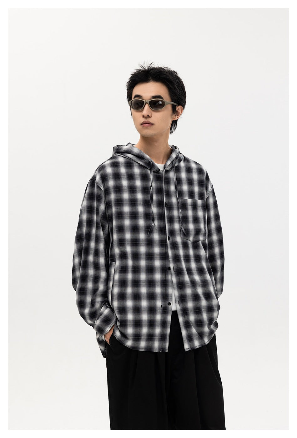 Model in black plaid hooded shirt jacket with chest pocket and drawstrings, hands in pockets, with sunglasses