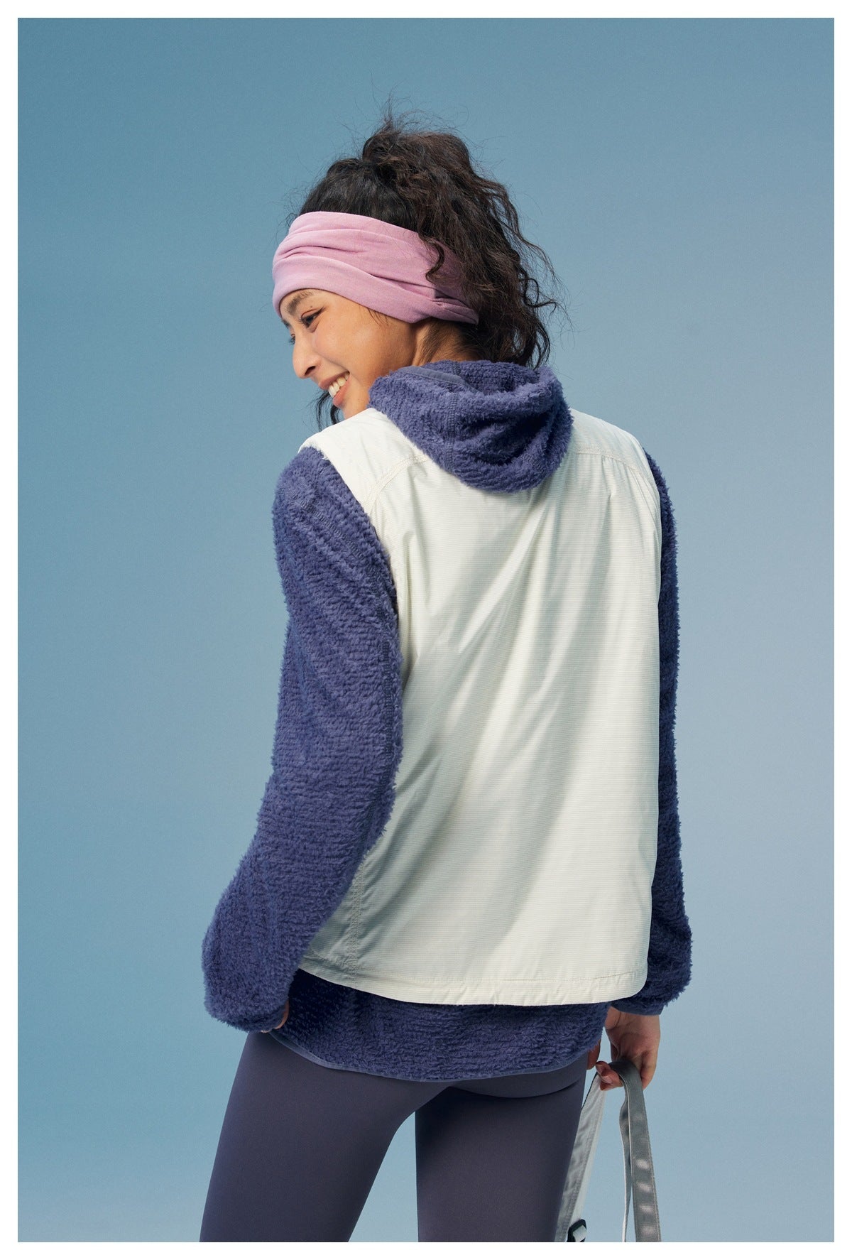 Rear view of a woman wearing a white-back pullover with navy fuzzy sleeves and hood, paired with a pink headband.