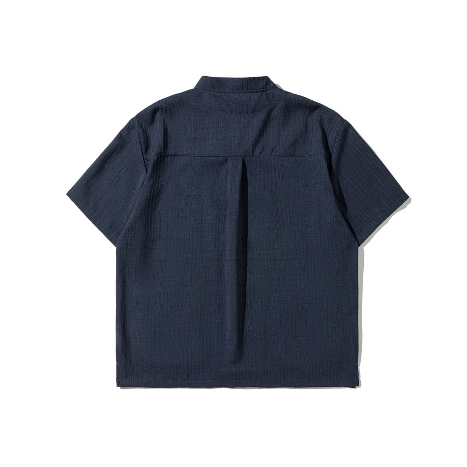 Back view of a navy short-sleeve shirt with a stand collar and center back pleat.