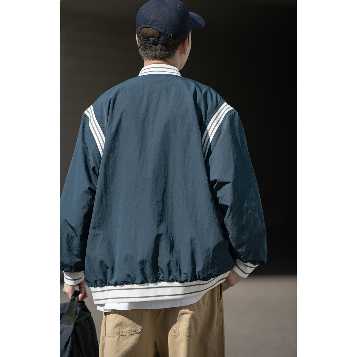 Back view of a model wearing a dark navy jacket with white striped shoulder, collar, cuff and hem trim.